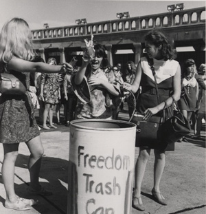 Women toss feminine items in a trash can as a form of protest about female oppression