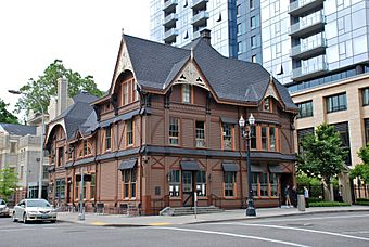 Photograph of a wooden building with peaked roofs on a city street corner.