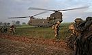 British soldiers prepare to board a Chinook twin-rotor helicopter landing on a field