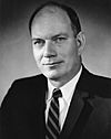 Black-and-white photo of a balding man in a suit and striped tie