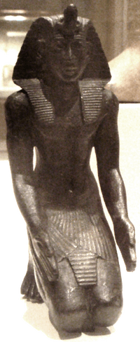 A small kneeling bronze statuette, likely Necho II, now residing in the Brooklyn Museum