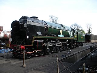 A posed side-and-front view of the rebuilt form of the locomotive, standing in the sidings of a locomotive depot. The locomotive is of conventional appearance, with a visible boiler and no flat covering plates. Smoke deflectors are fitted at the front of the locomotive.