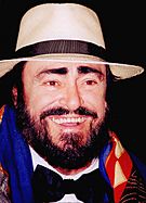 Pavarotti in a black bowtie, a white brimmed hat, a colourful scarf and a big smile.