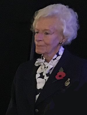Photograph of Mary Ellis. An elderly woman with white hair wearing a dark blue suit and a red British Legion poppy.
