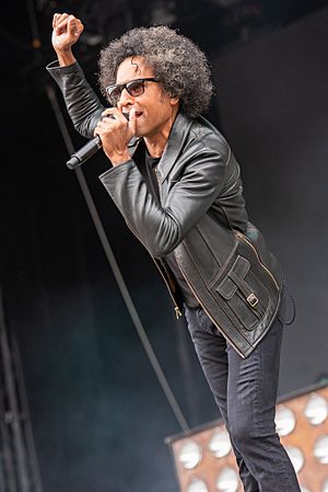 William DuVall wearing black jeans and leather jacket, standing onstage, singing into microphone with one hand raised up
