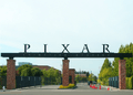 In the foreground is a paved street leading to the gate's entrance. A sign reading "PIXAR Animation Studios" sits on top of stone columns in front of the gate that leads to several buildings.