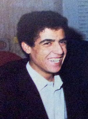 grainy image of a young Cheb Mami from profile, wearing a dark blazer and white shirt, grinning and looking at camera