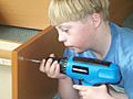 A boy with Down syndrome using cordless drill to assemble a book case