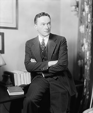 Lippmann wearing a suit, leaning against a desk with his arms crossed