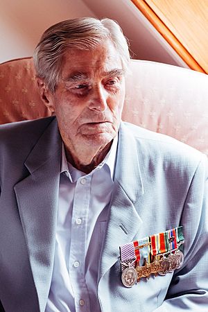 An elderly man, wearing various medals, looking towards something to the right of the camera.
