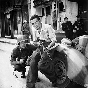 American officer and French partisan crouch behind an auto during a street fight in a French city. - NARA - 531322 - restored by Buidhe