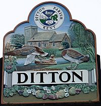 A photograph of a sign depicting an old church and ducks by a pond. The name of the village is shown above a row of flowers and fruit