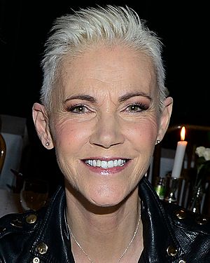 An image of a short-haired woman smiling in to a camera. There is a flame from a candle flickering above her left shoulder.