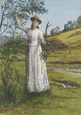 Eliza Ashton in a white dress standing under a wattle tree in a field of grass