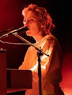 white female standing onstage, playing keyboard instrument and singing into microphone