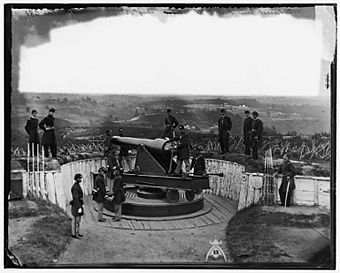 Historic photograph of a Union gun crew posed with a large cannon, behind earthwork fortifications and overlooking a large stretch of countryside