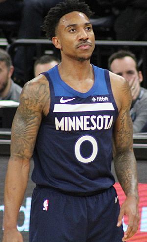 Portrait of man with dark hair and tattooed arms wearing navy blue Timberwolves uniform