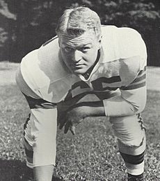 Posed photograph of Noll in a football uniform without a helmet in a three-point stance