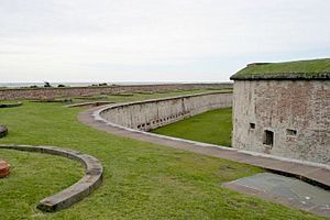 Ground-level color photograph (dated 2003) showing a portion of a wall of a building in the fort and the facing wall of the trench surrounding it.