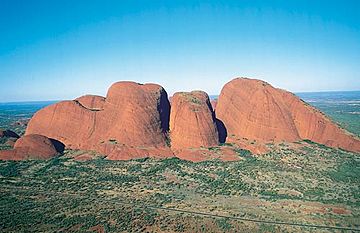 A series of red sandstone domes surrounded by scrub under a blue sky