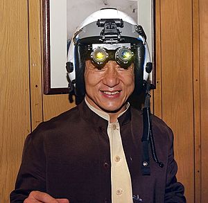 US Navy 021202-N-0271M-016 Jackie Chan tries on a fighter pilot's helmet with night vision goggles attached during his visit aboard USS Kitty Hawk (cropped)