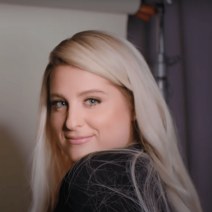 Meghan Trainor, a woman with platinum blonde hair, smiling and looking over her shoulder towards the camera