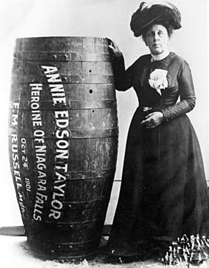 Black and white photo of Annie Edson Taylor standing next to a human-sized barrel