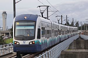 A train with four cars, traveling over a concrete bridge under catenary wires.