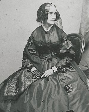 seated, black & white portrait of fifty-year-old woman wearing dark dress, hat with veil, glove on right hand