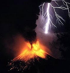 A photograph depicting a white bolt of lightning with a purple aura striking a volcano as it erupts yellow lava with a red aura and black smoke.