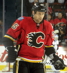 Upper body of a man staring intently into the distance.  He is in a full hockey uniform; the jersey is red with black and yellow trim, and a black stylized "C" logo on his chest.