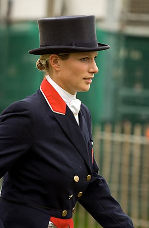 Lady pictured from waist up in formal riding habit of jacket with gold buttons and red flashes and top hat
