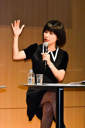 Author Mieko Kawakami seated at a table while speaking into a microphone