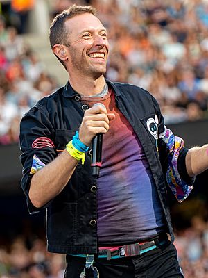 A short-haired man wearing a tye-die shirt and a dark-coloured jacket performs with a microphone