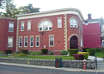 View of the library from across the street, with its retaining wall in front. It is a red brick building with some Italianate decoration and "Fowler Memorial Building" on the cream-colored frieze