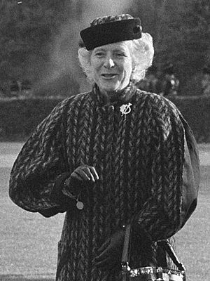 Candid cropped photo of Maeve Hillery walking away from a small aeroplane. Wearing a hat, heavy coat, gloves and carries a handbag. Also wearing a Tara Brooch.