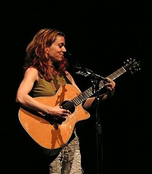 Ani Difranco standing onstage, playing an acoustic guitar