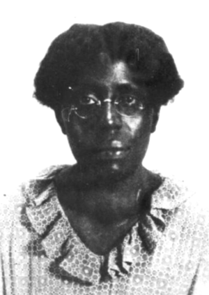 An African-American woman with short hair, wearing glasses and a dress with a ruffled collar