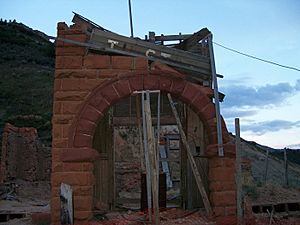 a mostly destroyed building with a sandstone arch entrance still standing. The arch is being propped up with wood to prevent its collapse. Above the doorway is a wooden sign that reads Thistle; some letters have fallen off.