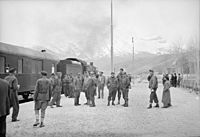 American and British soldier trainmen standing about at a station on the route for supplies to Russia. An American engine is seen at the head of the train at left, somewhere in Iran
