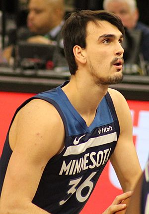 Chest high view of man with medium length dark hair, moustache and beard, preparing to shoot a free throw, wearing a navy blue Timberwolves uniform