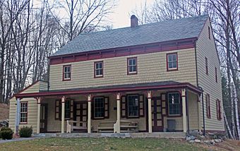 A two-story light yellow house with reddish trim, a pointed roof on the side, a small shed-roofed addition on the left and a porch along the front.