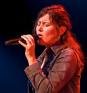 close-up of Paula Cole from profile, wearing a denim jacket, singing into a microphone with eyes closed