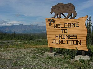 Photo of a large sign topped by a silhouette of a brown bear. The sign reads "Welcome to Haines Junction".