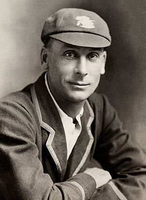 A black and white head and shoulders shot of a man wearing a cricket blazer and cap