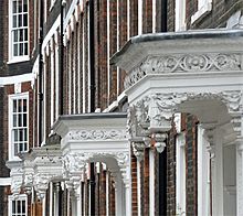 A row of ornate white porches hanging out from dark red brick houses.