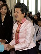 Tuenjai Deetes shaking hands with a woman at an event, smiling, wearing a pink jacket and scarf.