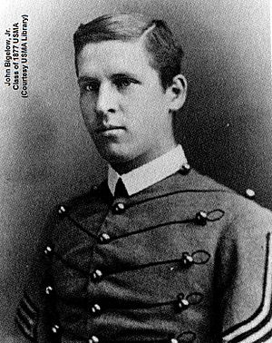 A black and white picture of John Bigelow Jr., a young white male in his United States Military Academy Cadet uniform. His Cadet uniform has a starched white collar and his tunic has large round brass buttons interconnected by hortizontal braiding. He is clean shaven with neatly combed short dark hair parted to his right. His right sleeve shows two stripes indicating he is a Cadet Lieutenant.