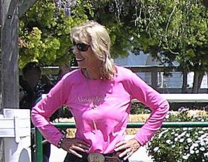 Sheila Varian; blonde caucasian woman wearing sunglasses and a pink shirt holding her hands on her hips and looking to her right