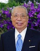 Daisaku Ikeda in a dark jacket, white shirt, light blue tie. Purple flowers fill the background.
